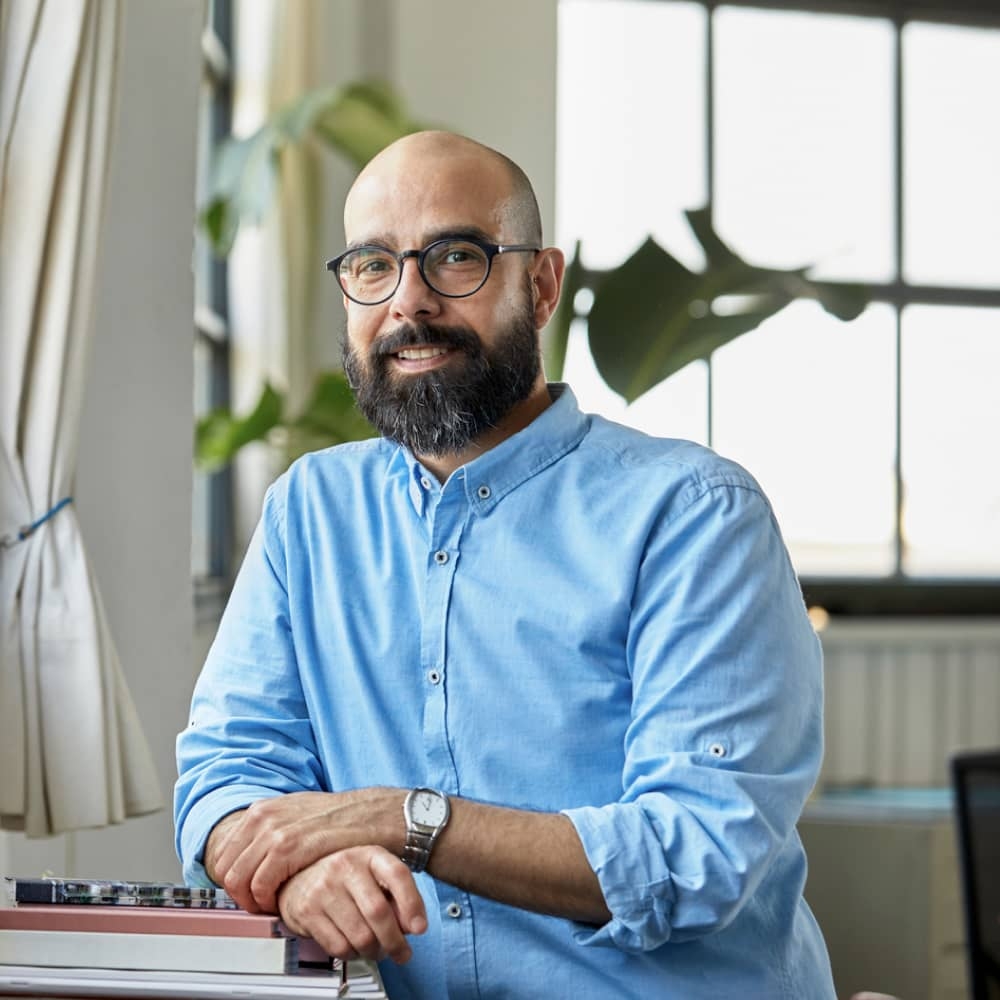 Man in blue shirt with glasses leaning on a surface and smiling