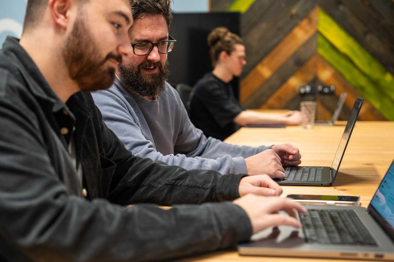 3 men at a desk working on laptops